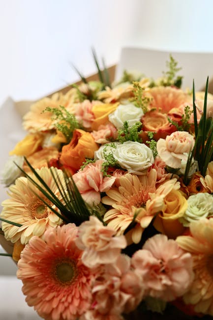 A vibrant floral bouquet featuring an assortment of fresh flowers including soft peach and pink gerbera daisies, delicate peach roses, light pink spray roses, and white lisianthus. The bouquet is acce